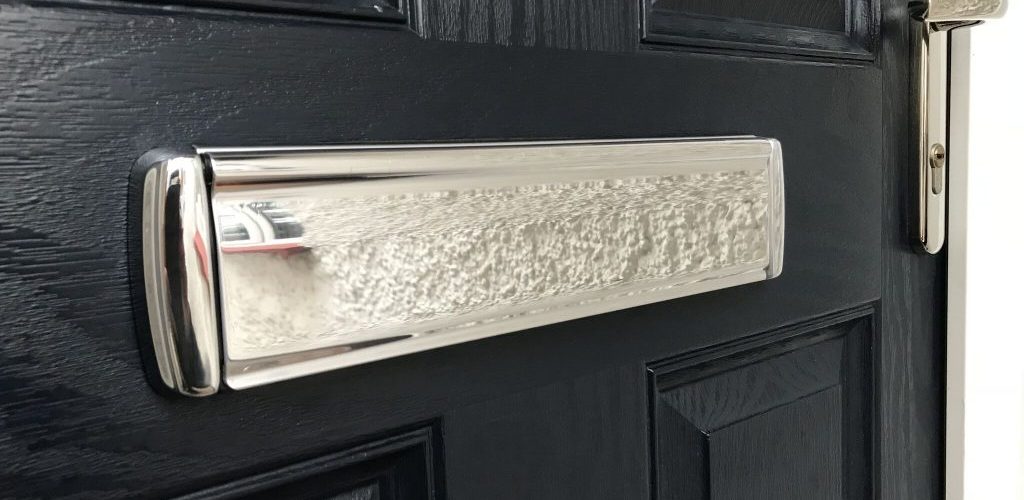 Close up of a polished chrome letterbox fitted to a black door