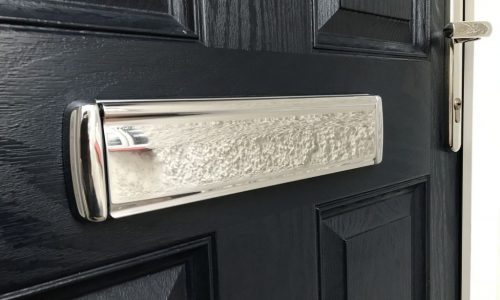 Close up of a polished chrome letterbox fitted to a black door